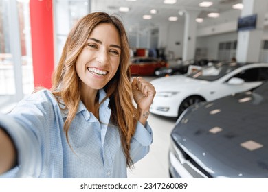 Close up woman customer buyer client in shirt do selfie shot pov on mobile phone do winner gesture choose auto want buy new automobile in car showroom vehicle salon dealership store motor show indoor. - Powered by Shutterstock