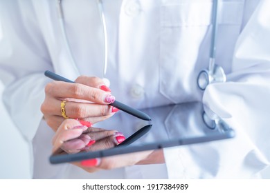 Close up of woman doctor hands using digital tablet at clinic. doctor in labcoat and stethoscope holding digital tablet, reading patient report.