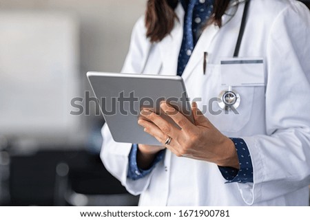 Close up of woman doctor hands using digital tablet at clinic. Closeup of doctor in labcoat and stethoscope holding digital tablet, reading patient report. Hands holding medical report, copy space.