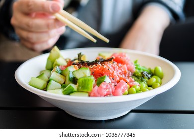 Nahaufnahme einer Frau, die Fischsalat-Poké-Schüssel mit Stäbchen isst