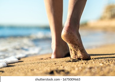 Close up of woman feet walking barefoot on sand leaving footprints on golden beach. Vacation, travel and freedom concept. People relaxing in summer.