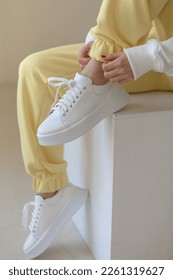 Close up of woman feet wearing training sneakers .female hands tie laces on sneakers. Female legs close-up, yellow joggers, white stylish sneakers.sports concept sports fashion
