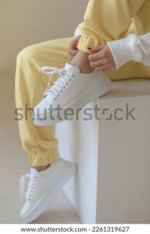 Close up of woman feet wearing training sneakers .female hands tie laces on sneakers. Female legs close-up, yellow joggers, white stylish sneakers.sports concept sports fashion