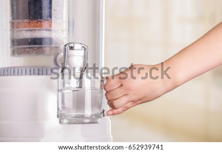 Close up of a woman filling a glass of water, with a filter system of water purifier on a kitchen background
