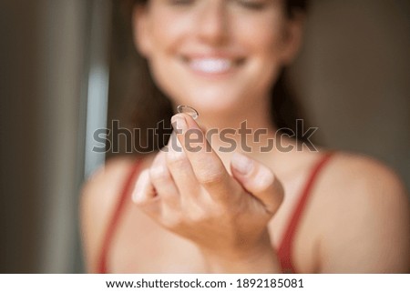 Close up of woman finger holding contact lens in front of her face.. Smiling young woman holding new contact lens on finger tip. Smiling girl holding contact lens, eyesight and eyecare concept.