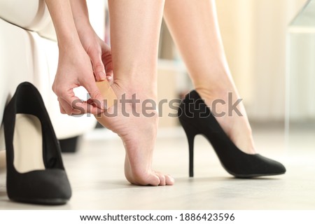 Close up of a woman foot in highheels putting a plaster on her heel at home
