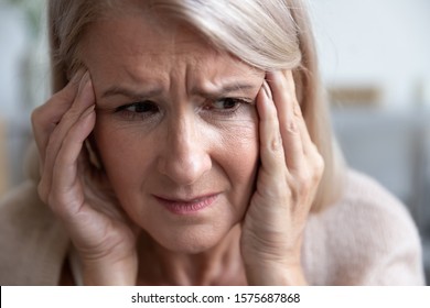 Close Up Woman Frown Face Holds Head With Hands Feels Desperate, 60s Female Touches Temples Suffers From Headache Thinking About Emotional Or Health Problems, Physical Decline Dementia Disease Concept