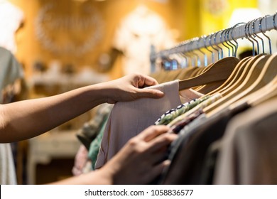 Close Up Of Woman Hand Choosing Thrift Young And Discount T-shirt Clothes In Store, Searching Or Buying Cheap Cotton Shirt On Rack Hanger At Flea Market , Stall Shopping Apparel Fashion Concept