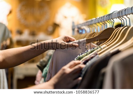 Close up of woman hand choosing thrift young and discount t-shirt clothes in store, searching or buying cheap cotton shirt on rack hanger at flea market , stall shopping apparel fashion concept