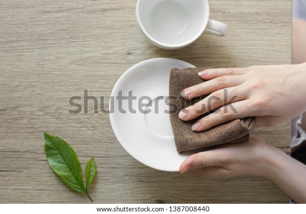 Close up woman hand cleaning coffee cup on the\
morning with microfiber cloth,Close up woman hand cleaning coffee\
cup on the rustic wood\
table.