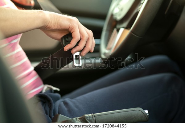 Close up of woman hand fastening seat
belt while sitting inside a car for safety before driving on the
road. Female driver driving secure and taking safe
jorney.