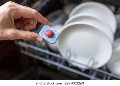 Close up of woman hand filling dishwasher tablet into open automatic stainless built-in dishwasher machine with dirty white dish inside in modern home kitchen.Household, housekeeping domestic life.