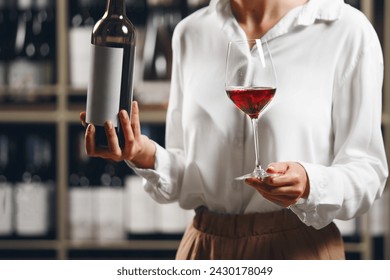 Close up woman hand hold bottle and glass with poured red wine on cellar background. - Powered by Shutterstock