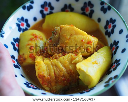 close up of woman hand hold a bowl of southern Thai spicy sour yellow curry with sea bass and durian