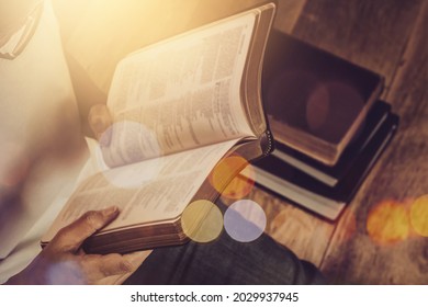 Close up of a woman hand  hold and reading the open bible, blurred page on wooden table with window light and Bokeh, Christian devotional, spiritual or bible study concept background with copy space - Shutterstock ID 2029937945