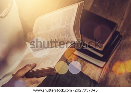 Close up of a woman hand  hold and reading the open bible, blurred page on wooden table with window light and Bokeh, Christian devotional, spiritual or bible study concept background with copy space