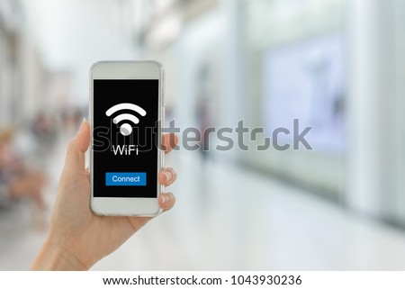 Close up woman hand hold smartphone connection to public WiFi hotspot in the city department store to access internet on smartphone WiFi Zone. Wireless technology and travel concept.