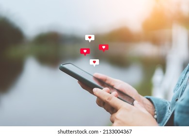Close up woman hand hold using smart phone with heart icon at outdoor park street background. Copy space of technology business and travel holiday concept. Vintage tone filter effect color style. - Shutterstock ID 2133004367