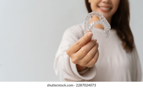 close up woman hand holding dental aligner retainer (invisible) on background for beautiful teeth and dental treatment course concept