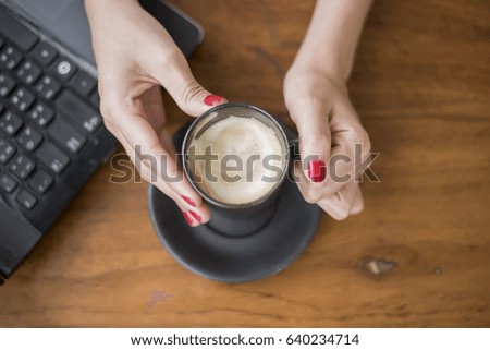 close up of woman hand holding hot coffee cup on wooden table