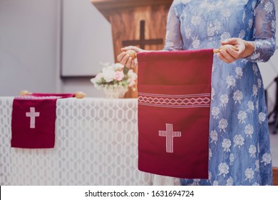 Close Up Of A Woman Hand Holding Red Offering Bag In Church, Focus On The White Cross In Offering Bog