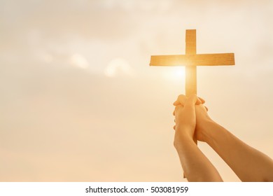  Close up woman hand holding wood cross or religion symbol shape over a sunset sky with clouds background for God,Christianity, religious, faith, holy, spiritual, Jesus, belief or resurrection.