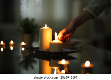 Cierre de la mano de una mujer encendiendo velas en la noche oscura en casa