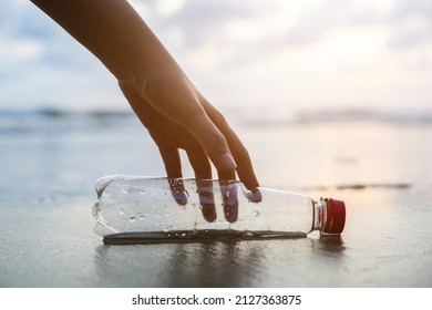 Close Up Woman Hand Pick Up The Plastic Bottle On The Beach. Female Volunteer Clean The Trash On The Beach Make The Sea Beautiful. World Environment Day Concept.