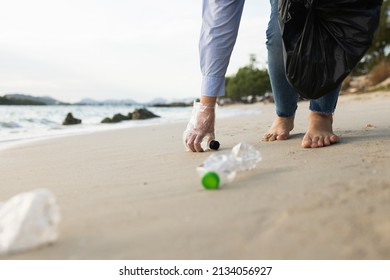 Close Up Woman Hand Pick Up The Plastic Bottle On The Beach. Female Volunteer Clean The Trash On The Beach Make The Sea Beautiful. World Environment Day Concept.