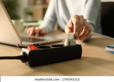 Close up of woman hand plugging plug on a power strip socket at night using laptop on a desk at home