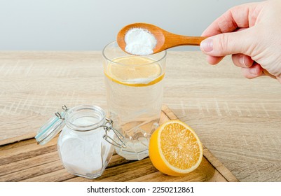 Close up of woman hand pouring baking soda in drinking glass with water and lemon juice, health benefits for digestive system concept. 