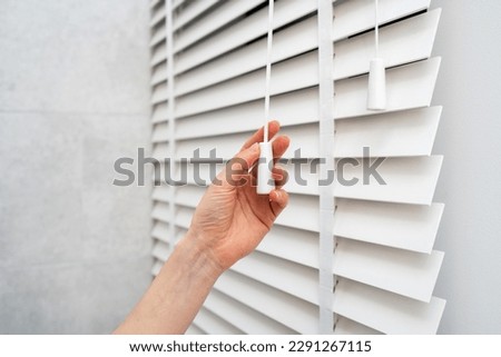 Close up woman hand pulls the adjustment string opening window blinds with wooden slats in tradition venetian style. Concept of jalousie in apartment room