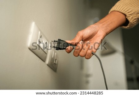 Close up woman hand put on or remove Electric plug cable in socket. Electrical equipment wires and power strips on the wall. Earth Hour saving  energy.