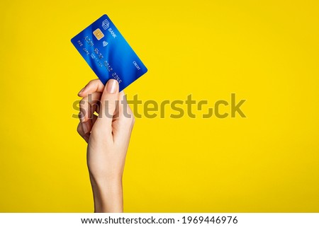 Close up of woman hand showing credit card on yellow background. Detail of female hand holding bank credit card against yellow wall with arm raised. Young woman showing creditcard with copy space.