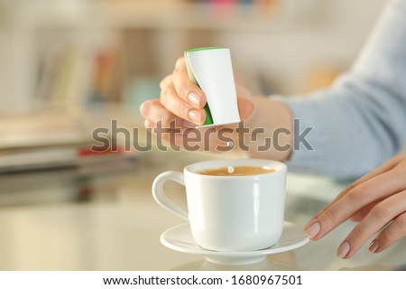 Close up of woman hand throwing saccharin pills on coffee cup on a desk at home