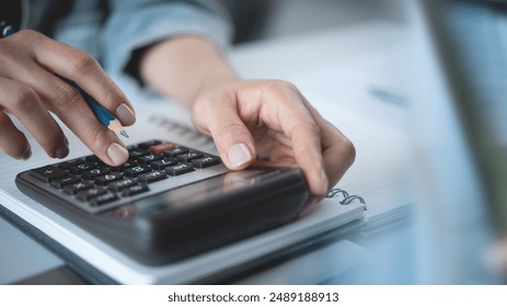 Close up woman hand using calculator to calculate home finance and writing note, accounting on table, budget management. Doing finance, budgeting and tax calculation, monthly expenses