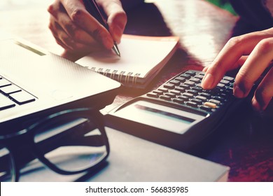 Close up woman hand using calculator and writing make note with calculate about cost at home office.