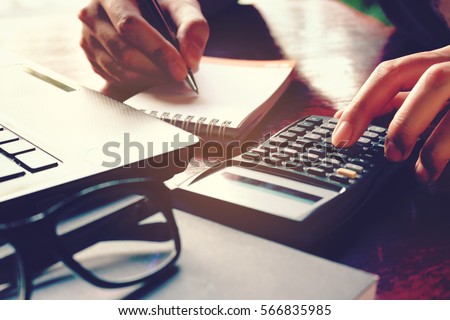 Close up woman hand using calculator and writing make note with calculate about cost at home office.