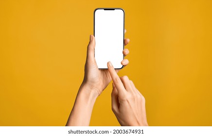 Cierre de la mano de una mujer usando un smartphone aislado en una pared naranja. Manos femeninas mostrando la pantalla blanca vacía del teléfono inteligente moderno. Mujer de negocios sostiene el celular y lo desbloquea con su huella dactilar.