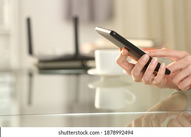 Close up of a woman hand using wifi on smart phone with a router in background at home