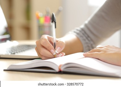Close up of a woman hand writing in an agenda on a desk at home or office