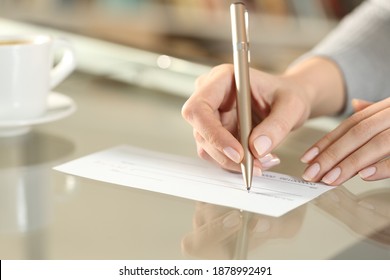 Close Up Of A Woman Hand Writing Bank Check To Make A Payment On A Table