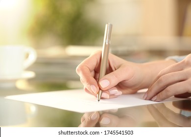 Close up of woman hand writing on a paper on a desk at home