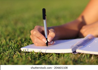 Close up of a woman hand writing on a notebook outdoor lying on the grass in a park - Powered by Shutterstock