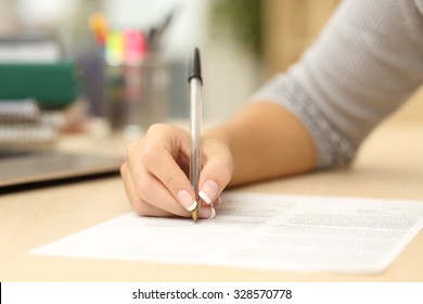 Close up of a woman hand writing or signing in a document on a desk at home or office