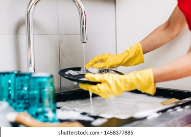 Close up of woman hand in yellow protective rubber gloves washing dishes in the kitchen.