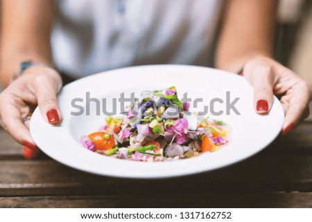 Close up of woman hands with beautiful nail polished carrying a white dish of spicy salad with pork.