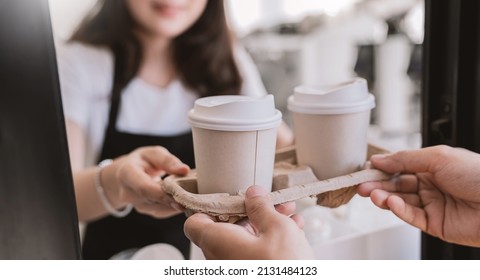 Close up woman hands gives paper coffee cup on slide glass window. Take away delivery concept. Asian woman barista. Cropped shot of waitress and buyer hold coffee, eco recycle environment friendly. - Shutterstock ID 2131484123