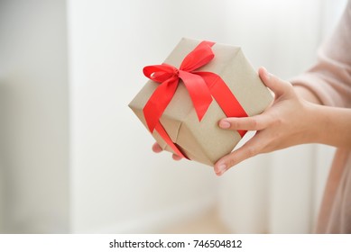 Close up woman hands holding a brown gift box with red ribbon for Birthday, Christmas and New year on white background. Copy space.