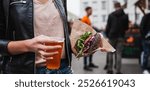 Close up of woman hands holding delicious organic salmon vegetarian burger and homebrewed IPA beer on open air beer an burger urban street food festival in Ljubljana, Slovenia